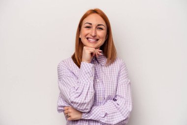 Beyaz arka planda izole edilmiş genç beyaz kadın mutlu ve kendinden emin gülümsüyor, elleriyle çenesine dokunuyor..