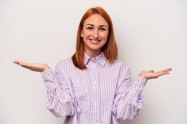 Beyaz arka planda izole genç beyaz kadın kollarıyla ölçek yapar, mutlu ve kendinden emin hisseder..