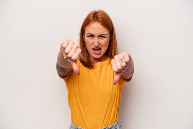 Beyaz arka planda izole edilmiş genç beyaz kadın baş parmağını aşağı gösteriyor ve hoşlanmadığını ifade ediyor..