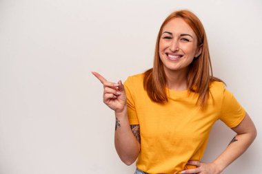 Beyaz arka planda izole edilmiş genç beyaz kadın işaret parmağıyla işaret ederek gülümsüyor..