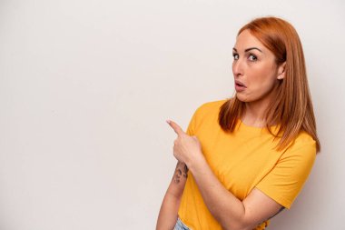 Beyaz arka planda izole edilmiş genç beyaz bir kadın gülümsüyor ve boş alanda bir şeyler gösteriyor..