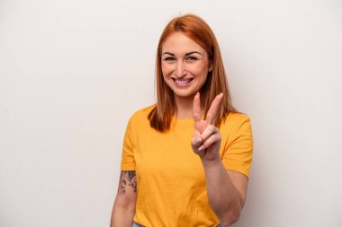 Beyaz arka planda izole edilmiş genç beyaz kadın zafer işareti gösteriyor ve gülümsüyor..