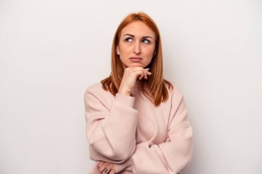 Beyaz arka planda izole edilmiş genç beyaz kadın şüpheli, belirsiz, seni muayene ediyor..