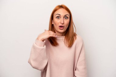 Beyaz arka planda izole edilmiş genç beyaz bir kadın bir şeye gülüyor, elleriyle ağzını kapatıyor..