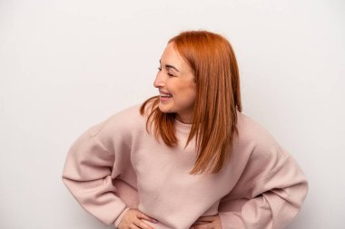 Beyaz arka planda izole genç beyaz kadın mutlu bir şekilde gülüyor ve ellerini karnının üstünde tutarak eğleniyor..