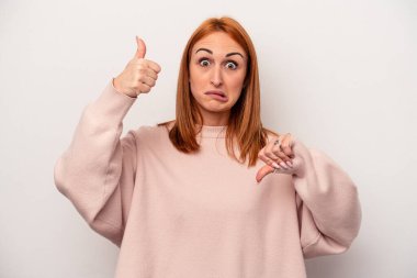Beyaz arka planda izole edilmiş genç beyaz bir kadın baş parmağını kaldırıyor ve baş parmağını aşağı gösteriyor, zor seçim konsepti.