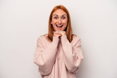 Beyaz arka planda izole edilmiş genç beyaz bir kadın şans için dua ediyor, şaşırmış ve ağzını açıp önüne bakıyor..