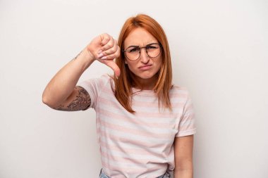 Beyaz arka planda izole edilmiş genç beyaz kadın baş parmağını aşağı gösteriyor ve hoşlanmadığını ifade ediyor..