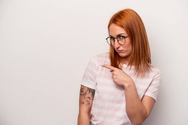 Beyaz arka planda izole edilmiş genç beyaz bir kadın gülümsüyor ve boş alanda bir şeyler gösteriyor..