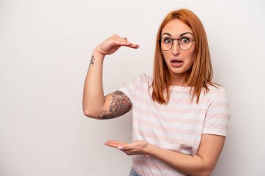 Beyaz arka planda izole genç beyaz kadın şok ve hayret içinde elleri arasında bir kopya alanı tutuyor.