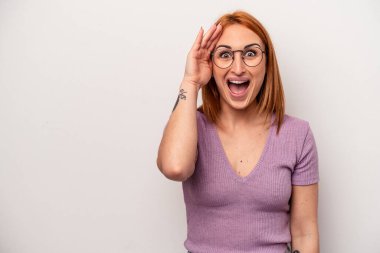 Beyaz arka planda izole genç beyaz kadın yüksek sesle bağırıyor, gözleri açık ve elleri gergin tutuyor..