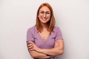 Beyaz arka planda kendini güvende hisseden, kararlılıkla kollarını kavuşturan beyaz tenli genç bir kadın..