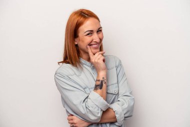 Beyaz arka planda izole edilmiş genç beyaz kadın mutlu ve kendinden emin gülümsüyor, elleriyle çenesine dokunuyor..