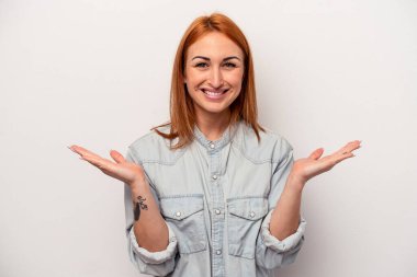 Beyaz arka planda izole genç beyaz kadın kollarıyla ölçek yapar, mutlu ve kendinden emin hisseder..