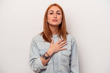 Beyaz arka planda izole edilmiş genç beyaz kadın yemin ediyor, elini göğsüne koyuyor..