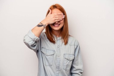 Beyaz arka planda soyutlanmış beyaz tenli genç bir kadın elleriyle gözlerini kapatıyor, geniş bir gülümsemeyle bir sürpriz bekliyor..