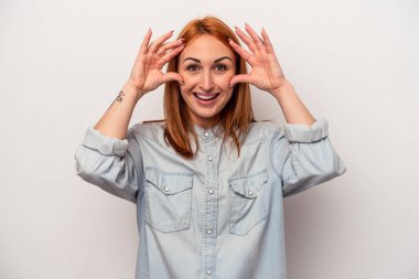 Beyaz arka planda izole genç beyaz kadın hoş bir sürpriz alıyor, heyecanlı ve el kaldırıyor..