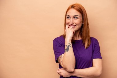 Beyaz tenli genç bir kadın, bej arka planda izole edilmiş. Rahatlamış, fotokopi odasına bakan bir şey düşünüyor..