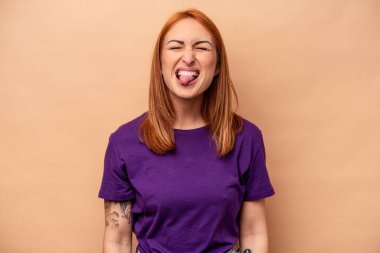 Beyaz tenli genç bir kadın bej arka planda izole edilmiş komik ve dost canlısı bir dil kullanıyor..