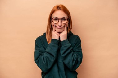 Beyaz tenli genç bir kadın bej arka planda izole edilmiş. İki seçenek arasında şüpheyle bakıyor..