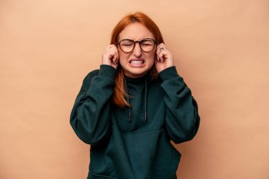 Beyazlı genç bir kadın bej arka planda izole edilmiş kulakları elleriyle kapatıyor..