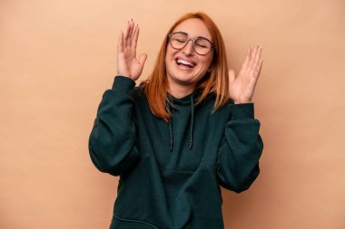 Beyaz tenli genç bir kadın, bej arka planda izole edilmiş neşeli bir şekilde gülüyor. Mutluluk kavramı.