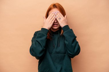 Beyazlı genç bir kadın bej arka planda izole edilmiş. Gözleri elleriyle kapamaktan korkuyor..