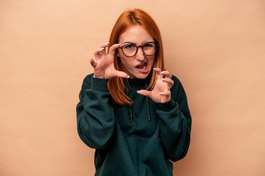 Bej arka planda izole edilmiş beyaz bir kadın pençelerini kedi taklidi yaparken gösteriyor, agresif bir hareket..