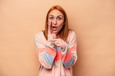 Beyaz tenli genç bir kadın bej arka planda izole edilmiş. Dedikodu yapıyor, bir şeyleri bildiriyor..