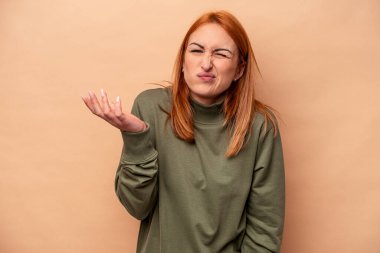 Beyaz tenli genç bir kadın bej arka planda izole edilmiş sorgulama sırasında omuz silkiyor ve şüphe duyuyor..