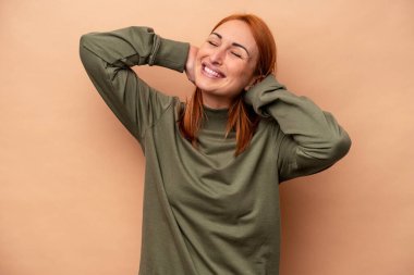 Beyaz tenli genç bir kadın bej arka planda izole edilmiş, kendinden emin, elleri başının arkasında..