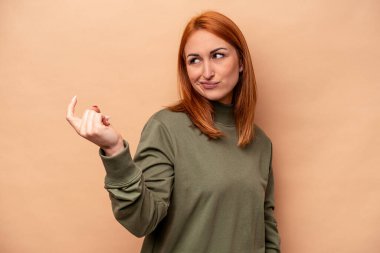 Beyaz tenli genç bir kadın, bej arka planda izole edilmiş. Seni işaret ediyor. Sanki davet ediliyormuş gibi..