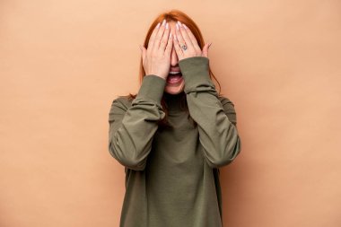 Beyaz tenli, bej arka planda izole edilmiş genç bir kadın yüzünün yarısını palmiye ile örterek eğleniyor..