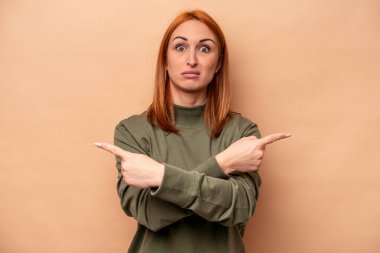 Beyaz tenli genç bir kadın bej arka planda iki seçenek arasından seçim yapmaya çalışıyor..