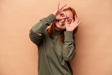 Beyazlı genç bir kadın bej arka planda izole edilmiş, gözlerde sorun yok işareti var.