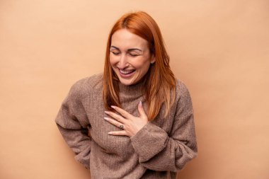 Beyaz tenli genç bir kadın bej arka planda izole edilmiş. Gülüyor, elini kalbe koyuyor, mutluluk kavramını koruyor..