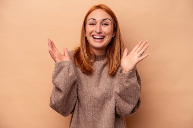 Beyaz tenli genç bir kadın, bej arka planda izole edilmiş. Yüksek sesle gülüyor, elini göğsüne koyuyor..