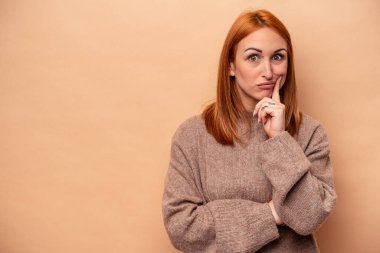 Beyazlı genç bir kadın bej arka planda izole edilmiş şüpheli ve şüpheci bir ifadeyle yana bakıyor..