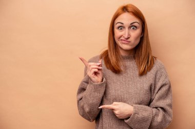 Beyazlı genç bir kadın bej arka planda izole edilmiş. İşaret parmaklarıyla bir fotokopi alanını işaret ederek şok olmuş..