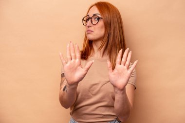 Beyaz tenli genç bir kadın bej arka planda izole edilmiş, elini uzatmış, dur işareti gösteriyor, bu da seni engelliyor..