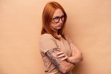 Beyazlı genç bir kadın bej arka planda izole edilmiş hoşnutsuzca kaşlarını çatmış, kollarını kavuşturmuş..