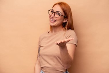 Beyaz tenli genç bir kadın bej arka planda izole edilmiş. Kameraya elini uzatarak selam veriyor..