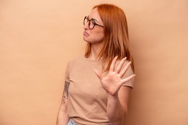Beyaz tenli genç bir kadın, bej arka planda izole edilmiş. İğrenme belirtisi gösteren birini reddediyor..