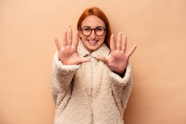 Beyazlı genç bir kadın bej arka planda izole edilmiş. Elleriyle on numarayı gösteriyor..