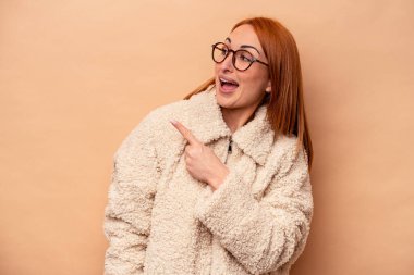 Beyaz tenli genç bir kadın bej arka planda izole edilmiş. Gülümsüyor, neşeli ve hoş görünüyor..