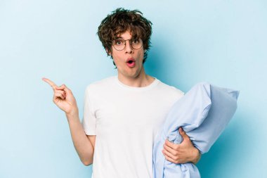 Genç beyaz bir adam pijama giyiyor ve yastığı mavi arka planda yalnız tutuyor.