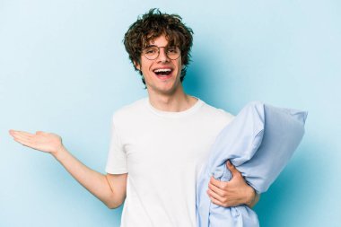 Genç, beyaz bir adam pijama giyiyor ve yastığı mavi arka planda tutuyor. Bir avuç içinde fotokopi alanı var ve belinde başka bir el tutuyor..