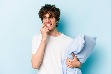 Genç beyaz bir adam pijama giyiyor ve yastığı mavi arka planda yalnız tutuyor. Bir şeyin fotokopi odasına baktığını düşünerek rahatlıyor..