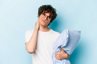 Genç beyaz bir adam pijama giyiyor ve yastığı mavi arka planda yalnız tutuyor. Kafasının arkasına dokunuyor, düşünüyor ve bir seçim yapıyor..