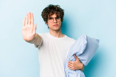 Genç, beyaz bir adam pijama giyiyor ve yastığı mavi arka planda yalnız tutuyor. Elini uzatmış, dur işaretini göstererek seni engelliyor..